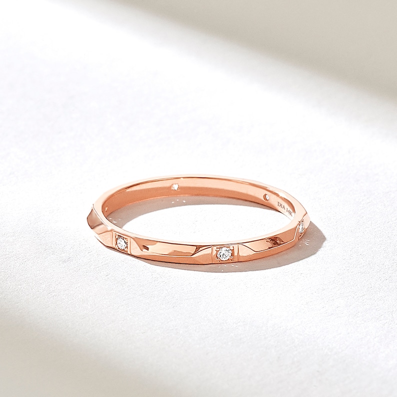 May include: A rose gold band ring featuring a faceted geometric surface with small round clear stones set at intervals. The interior of the band is clearly engraved with the text DIA 14K, indicating the metal composition of the jewelry piece.