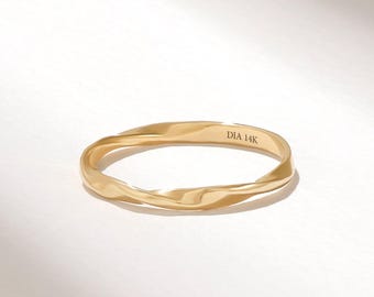 Puede incluir: Un anillo de oro con un diseño de banda retorcida y ondulada. La superficie interior del anillo está claramente grabada con el texto DIA 14K, indicando la composición del metal. El anillo presenta un acabado pulido y reflectante en toda su estructura.