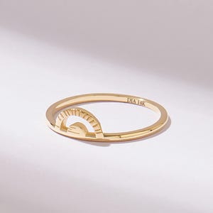Op de afbeelding: Een dunne gouden ring met een klein, verhoogd halfrond zonnestraalontwerp op de band. De binnenkant van de ringband is duidelijk gegraveerd met de tekst DIA 14K, wat de metaalsamenstelling van dit gepolijste geelgouden sieraad aangeeft.