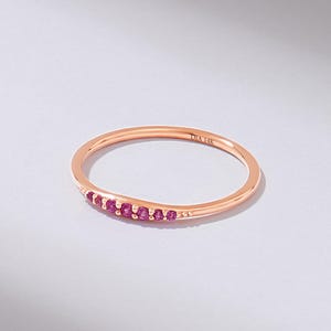 Puede incluir: Anillo de oro rosa con una banda delicada, engastado con peque&ntilde;as gemas rosas vibrantes. El anillo est&aacute; marcado "DIA 14K". Las gemas est&aacute;n agrupadas en un lado del anillo, creando un dise&ntilde;o sutil y elegante.