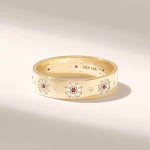 May include: A 14K gold band ring featuring a repeating pattern of star-shaped clusters, each centred with a small red gemstone surrounded by clear white stones. The interior of the band is clearly engraved with the text DIA 14K.