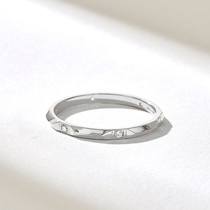 May include: A silver-toned metal band ring featuring a series of small, clear, round-cut stones set at intervals along the outer surface. The interior of the band is clearly engraved with the text DIA 14K, indicating the metal composition.