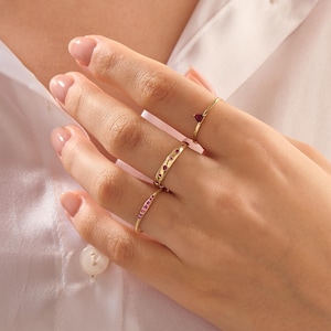 Puede incluir: Una mano con cuatro anillos de oro. Un anillo tiene una gema roja triangular, otro tiene una fila de peque&ntilde;as gemas rojas y un tercero tiene recortes en forma de coraz&oacute;n con gemas rojas. El cuarto anillo tiene una fila de peque&ntilde;as gemas rojas.