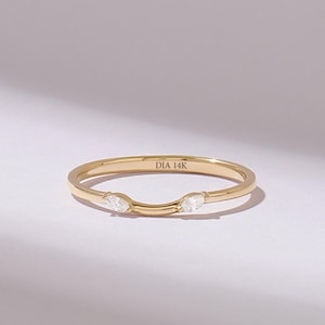 Op de afbeelding: Een gouden ring met een gebogen band voorzien van twee heldere marquise-geslepen stenen aan weerszijden van de centrale dip. De binnenkant van de band is duidelijk gegraveerd met de tekst DIA 14K, wat de metaalzuiverheid en diamant aangeeft.