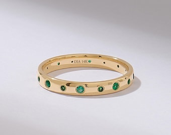 May include: A gold band ring featuring multiple small, round, bezel-set green gemstones spaced evenly around the exterior. The interior of the band is clearly engraved with the text DIA 14K, indicating the metal purity of the jewelry piece.