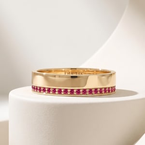 Könnte beinhalten: Ein goldener Bandring mit einer Reihe kleiner, runder, leuchtend pinker Edelsteine entlang der unteren Kante. Die Innenseite des polierten Goldrings ist deutlich mit dem Text DIA 14K graviert, was den Reinheitsgrad des Metalls angibt.