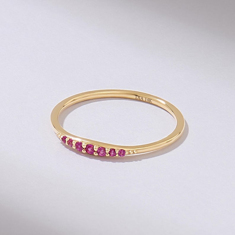 May include: A thin gold band with a row of small pink gemstones set along the top. The band is inscribed with 'DIA 14K'.