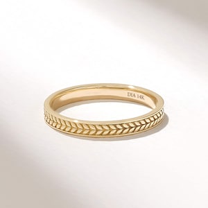 Puede incluir: Un anillo de banda de oro con un patrón grabado continuo de hojas o trigo alrededor del exterior. El interior de la banda está claramente marcado con el texto DIA 14K, indicando la composición metálica de esta joya de oro amarillo pulido.
