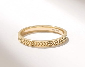 Puede incluir: Un anillo de banda de oro con un patrón grabado continuo de hojas o trigo alrededor del exterior. El interior de la banda está claramente marcado con el texto DIA 14K, indicando la composición metálica de esta joya de oro amarillo pulido.