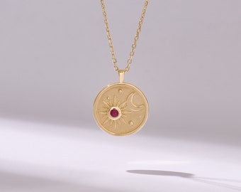 Pode incluir: Colar de ouro com um pingente redondo que apresenta um design de sol e lua com uma pedra preciosa vermelha no centro.