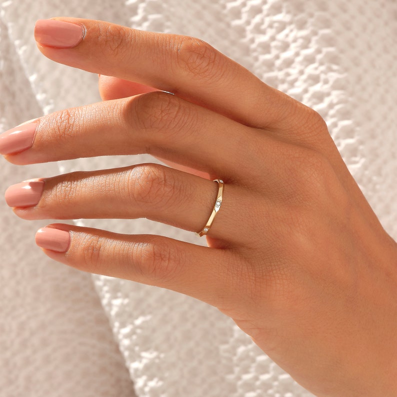 May include: A thin gold band ring with five small, clear gemstones set in the band.
