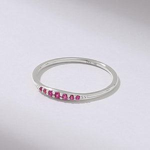 Puede incluir: Un delicado anillo de plata con una fila de peque&ntilde;as y vibrantes piedras preciosas rosas. El anillo tiene una banda delgada y est&aacute; marcado con "DIA 14K". Las piedras preciosas est&aacute;n muy juntas, creando una l&iacute;nea continua de color.