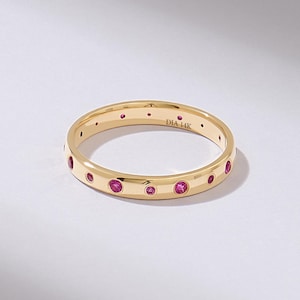 May include: A gold band ring featuring a series of flush-set round pink gemstones spaced evenly around the exterior. The interior of the band is engraved with the text DIA 14K, indicating the metal purity and material composition of the jewellery.