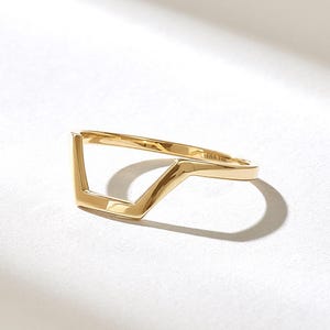 以下が含まれることがあります： V字型の幾何学的なデザインが特徴の光沢のあるゴールドリング。バンドは滑らかで反射する表面を持ち、内側には金属の組成を示すDIA 14Kという刻印が施されています。このジュエリーはシンプルで洗練された形状をしています。