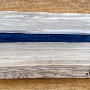 May include: A rectangular wooden cutting board with a blue epoxy resin inlay. The board has a natural wood grain pattern and is branded with "FAT CAT" in the lower right corner.