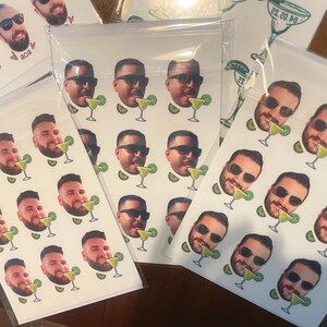 May include: A sheet of white stickers with multiple images of people's faces with a margarita glass in front of them. The stickers are printed with a white background and the images are in color.