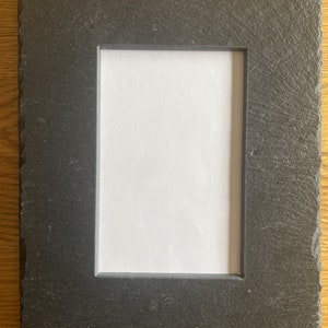 Op de afbeelding: Een zwart leisteen fotolijst met een ruw, getextureerd oppervlak. De lijst heeft een rechthoekige opening voor een foto.
