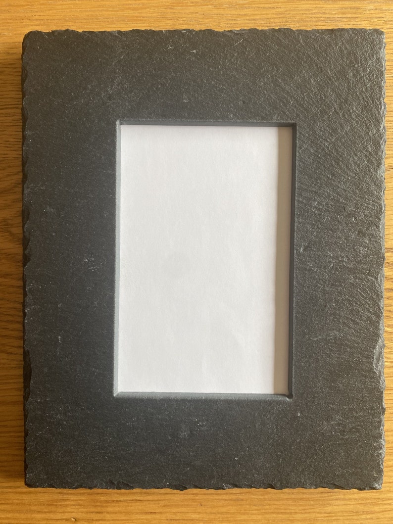 Op de afbeelding: Een zwart leisteen fotolijst met een ruw, getextureerd oppervlak. De lijst heeft een rechthoekige opening voor een foto.