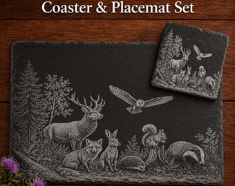 May include: Slate Woodland Coaster & Placemat Set. The set includes a rectangular placemat and a square coaster, both black with a detailed engraved woodland scene. The scene features a deer, fox, rabbit, owl, squirrel, and badger. The text "Slate Woodland Coaster & Placemat Set" is at the top.