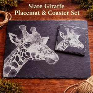 May include: Slate giraffe placemat and coaster set. The set features a detailed engraving of a giraffe's head on a rectangular placemat and a square coaster. The text "Slate Giraffe Placemat & Coaster Set" is at the top.