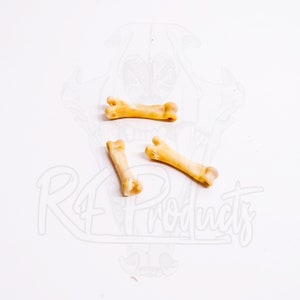 May include: Four tan-colored bone-shaped objects are arranged on a white surface. The objects have a natural bone appearance, with a slightly curved shape and rounded ends. The background features a faint illustration and the text "RF products".