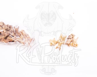 May include: A close-up of a bag of small, light brown animal bones. There are also a few bones scattered on a white surface.
