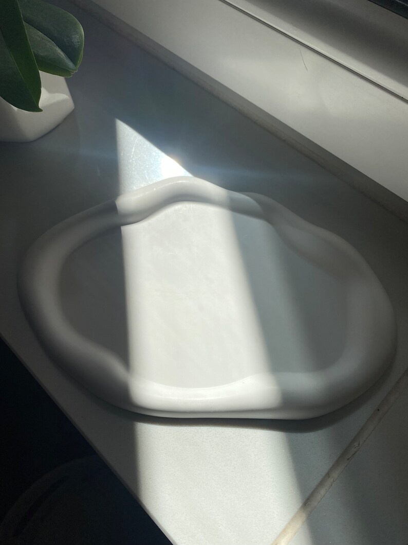 Peut inclure: Plateau en c&eacute;ramique blanche de forme ondul&eacute;e et organique. Le plateau pr&eacute;sente une d&eacute;pression arrondie peu profonde au centre.