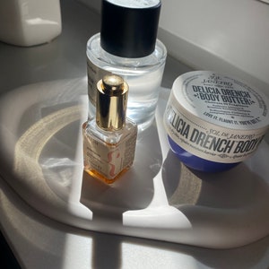 Peut inclure: Trois produits de beaut&eacute; sur un plateau en c&eacute;ramique blanche. Un flacon en verre transparent avec un bouchon noir et une &eacute;tiquette dor&eacute;e qui dit "A Very Remarkable Peach". Un petit flacon en verre ambr&eacute; avec un bouchon dor&eacute; et une &eacute;tiquette qui dit "Intensive Serum". Un pot blanc avec un couvercle bleu et une &eacute;tiquette qui dit "Sol de Janeiro Delicia Drench Body Butter".