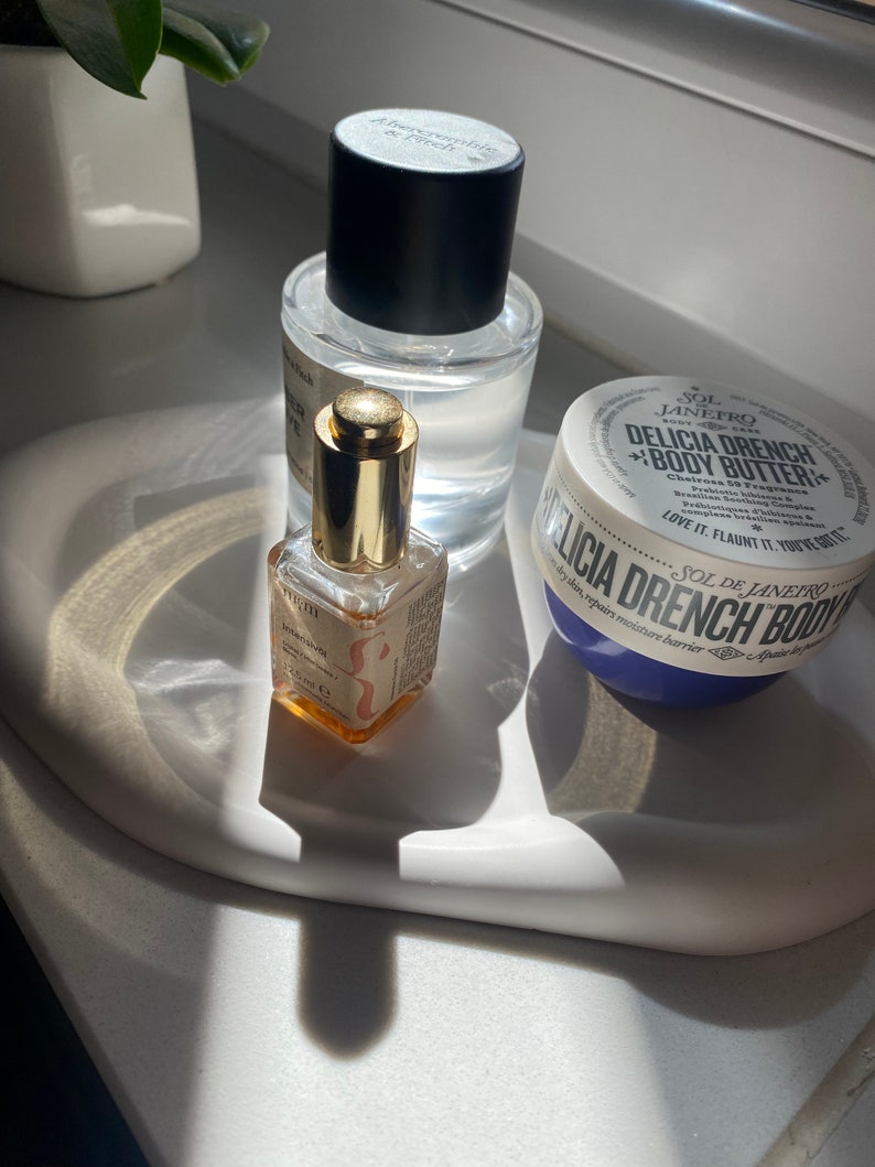 Peut inclure: Trois produits de beaut&eacute; sur un plateau en c&eacute;ramique blanche. Un flacon en verre transparent avec un bouchon noir et une &eacute;tiquette dor&eacute;e qui dit "A Very Remarkable Peach". Un petit flacon en verre ambr&eacute; avec un bouchon dor&eacute; et une &eacute;tiquette qui dit "Intensive Serum". Un pot blanc avec un couvercle bleu et une &eacute;tiquette qui dit "Sol de Janeiro Delicia Drench Body Butter".