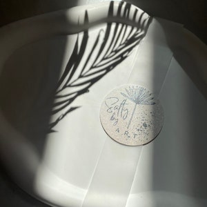 Peut inclure: Un plateau de service en c&eacute;ramique blanche avec un autocollant rond qui dit "Salty by ART" dans une police d'&eacute;criture manuscrite. L'autocollant a un motif de pissenlit noir et blanc et un fond mouchet&eacute;.