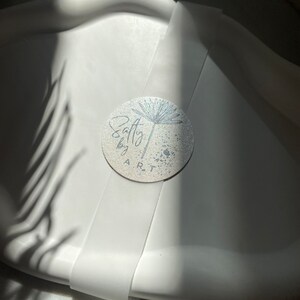 Peut inclure: Un plateau en c&eacute;ramique blanche avec un autocollant argent&eacute; repr&eacute;sentant une fleur stylis&eacute;e et le texte "Salty by ART".