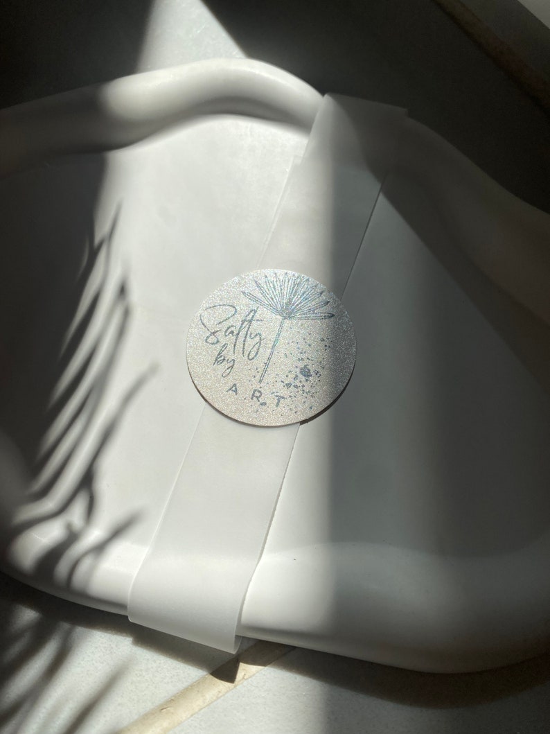Peut inclure: Un plateau en c&eacute;ramique blanche avec un autocollant argent&eacute; repr&eacute;sentant une fleur stylis&eacute;e et le texte "Salty by ART".