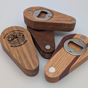 Op de afbeelding: Drie houten flessenopeners met een metalen opener. Een opener heeft de tekst "Pacific Northwest Wonderland" met een berglandschap in een cirkel. De andere twee openers hebben een houtnerfpatroon met een donkere houtinleg.