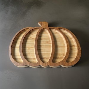 Puede incluir: Una bandeja de servir de madera con forma de calabaza con cinco secciones. La bandeja está hecha de madera marrón claro con un acabado natural.