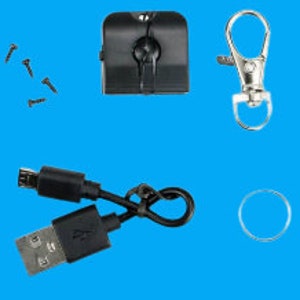 Może przedstawiać: Czarna kamera szpiegowska z wbudowanym brelokiem, kablem ładującym USB, czterema śrubami, metalowym kółkiem do kluczy i srebrnym karabińczykiem.