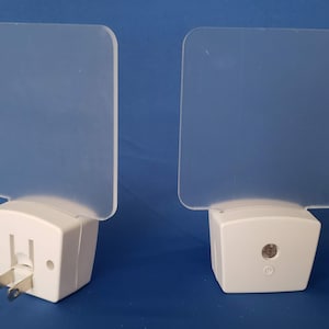 May include: Two white plug-in night lights with frosted square-shaped light covers. The lights have a small sensor on the front and a power switch on the side.