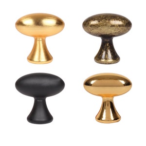 May include: Four cabinet knobs in different finishes: gold, antique brass, black, and polished gold. Each knob has an oval top and a rounded base.