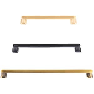 May include: Three cabinet pulls in different finishes: gold, black, and antique brass. Each pull is rectangular with a square end cap and the word "Gilroy" engraved on the top.
