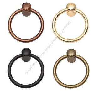 Pode incluir: Quatro puxadores de anel de metal diferentes com um botão redondo. Os puxadores são de cor preta, cobre, dourado e latão antigo.