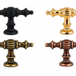 May include: Four T-shaped cabinet knobs arranged in a grid. Each knob features a central fluted barrel, pointed finials on the ends, and a circular base. The finishes include matte black, polished gold, antique brass, and a dark copper tone.