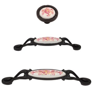 May include: A set of three cabinet hardware pieces: a round knob and two elongated pulls. Each piece features a white ceramic insert with a pink and yellow floral design, set within a dark brown metal frame. The pulls have ornate, curved handles.