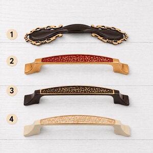 May include: Four cabinet pulls arranged vertically. Number 1 is a dark brown ornate pull. Number 2 is a gold pull with a red textured inlay. Number 3 is a dark brown pull with a black textured inlay. Number 4 is a cream pull with a white textured inlay.