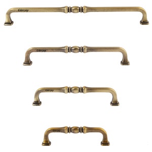 Op de afbeelding: Vier antieke gouden kastdeurgrepen met een decoratief ontwerp. De grepen zijn in verschillende maten en hebben het woord "Gurcay" erop gegraveerd.