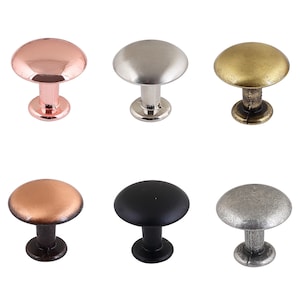 May include: Six different colored cabinet knobs. The knobs are round and have a mushroom shape. The colors are rose gold, silver, brass, black, and two shades of gray.