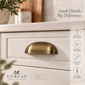 May include: A brass-toned, semi-circular cup drawer pull mounted on a white cabinet. Text reads: Small Details. Big Difference. GÜRCAY HOME HARDWARE. BEAUTIFUL HOMES LAST LONGER. Icons indicate premium zinc alloy, multiple finishes, sizes, and screws included.