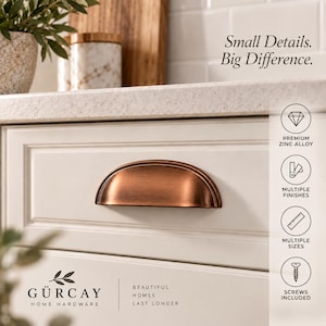 May include: A semi-circular cup drawer pull in a brushed copper finish mounted on a white cabinet drawer. The image includes the text Small Details. Big Difference. and GÜRKAY HOME HARDWARE, along with icons for zinc alloy, finishes, sizes, and screws.