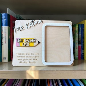 May include: A light-colored wooden picture frame featuring the white text "Mrs. Katona" at the top, a yellow pencil-shaped plaque with the text "BEST TEACHER EVER," and the engraved message "Thank you for the love, patience and care you have given our kids. -The Pelz Family."