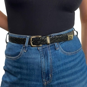 May include: A black belt with a textured snakeskin pattern and a rectangular antique brass buckle. The belt features a matching brass-toned metal loop and a rectangular metal tip at the end, worn through the belt loops of blue denim jeans.