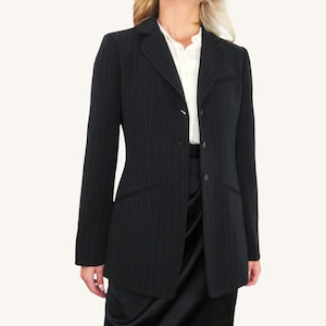 May include: A black pinstripe blazer with a two-button closure and notched lapels. The blazer has two front pockets and a tailored fit. The model is wearing a white collared shirt underneath. The blazer is a classic piece of business attire.