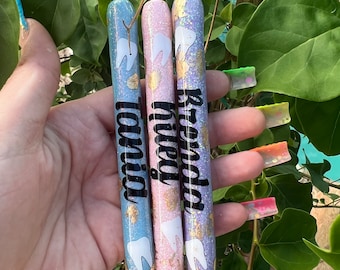 May include: Three glitter pens with black ink and white tooth designs. The pens are blue, pink, and gold. The names "Brenda", "Nikki", and "Tonja" are written on the pens.